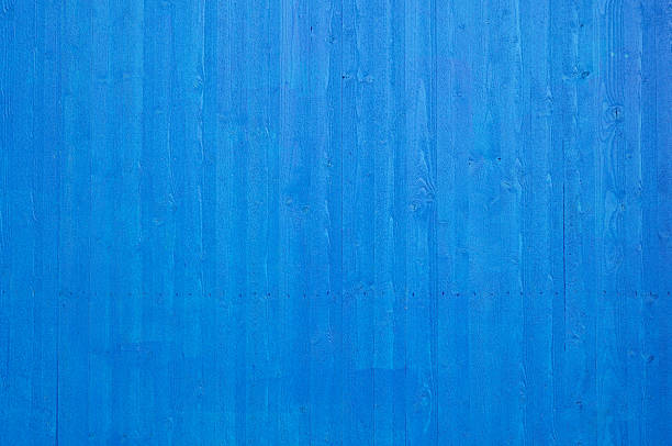 Fresh newly painted blue wooden plank wall with vertical planks surrounding a building / construction site. Nails visible.