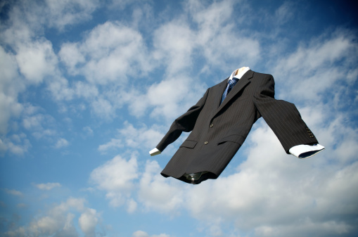 Empty dark suit floats in the sky in front of puffy clouds