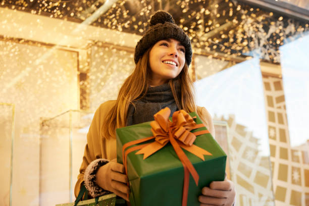 istock Gift in her grasp: The woman holds a gift with both hands surrounded by Christmas lights. 1824168018