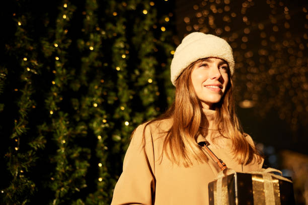 istock Captured from below, the woman smiles and holds a wrapped gift with a bow while looking into the distance. 1824170855
