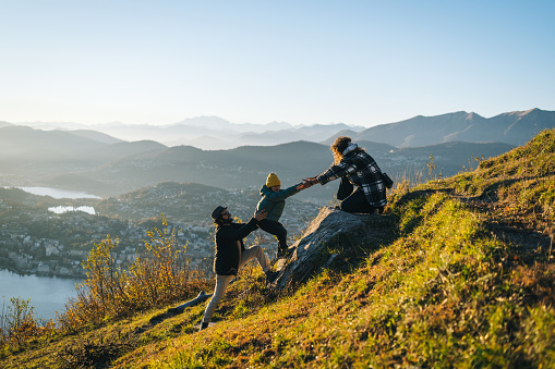 Mother offers helping hand to son on mountain top and father helps below