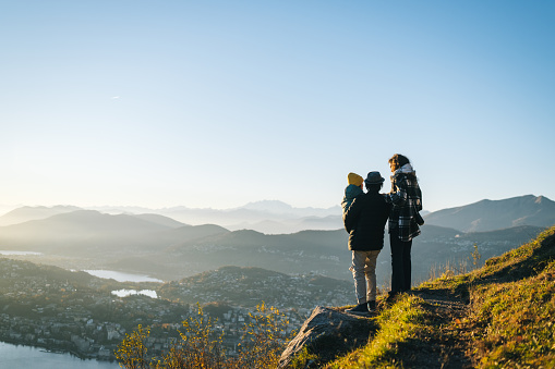 Family stands on mountain top together at sunset and looks out to lake