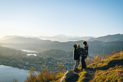 Family stands on mountain top together at sunset and looks out to lake