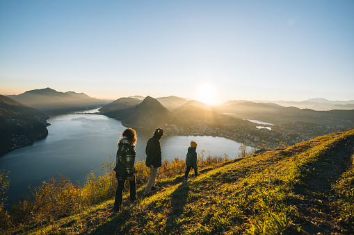 Family walks along mountain top above lake together at sunset