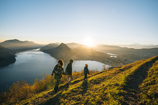 Family walks along mountain top above lake together at sunset