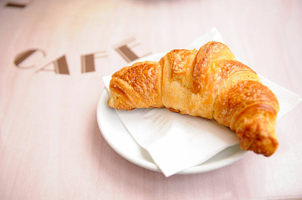 A real French croissant on French Cafe's terrace table. The work 'Cafe' is written on the table. Shallow depth of field.