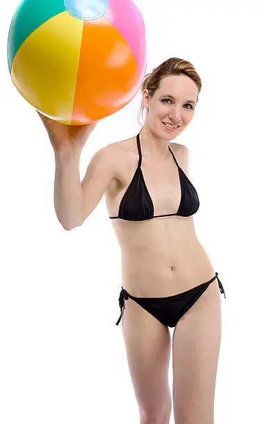 A young attractive woman in a bikini poses with a beach ball in the studio on white.