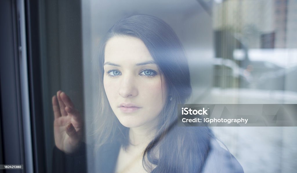 Joven mujer mirando por la ventana con nostalgia - Foto de stock de 18-19 años libre de derechos