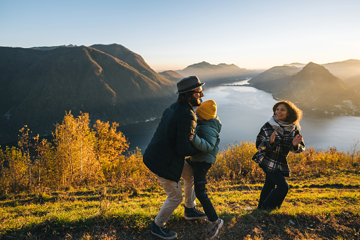 Family runs along mountain top above lake together at sunset