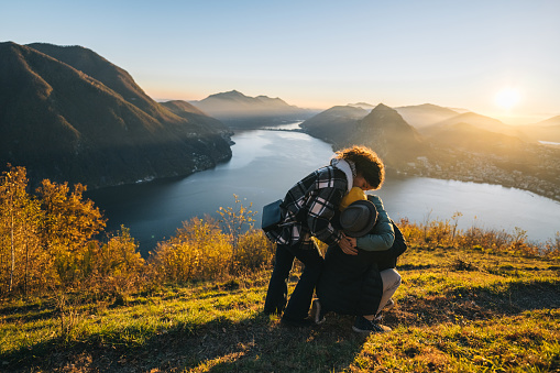 Family embraces on mountain top above lake at sunset