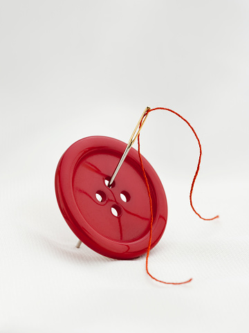 red button and needle isolated over white fabric