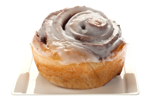 A cinnamon bun on a white background. Selective focus on front of bun