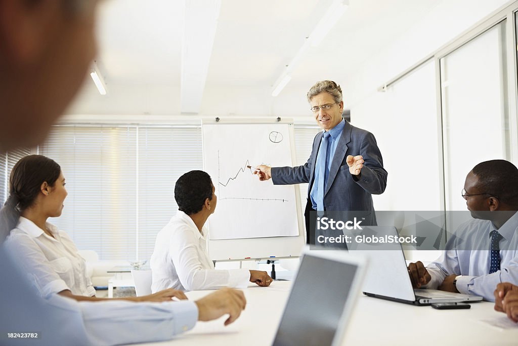 Business man explaining financial chart to colleagues Mature business man explaining financial chart during a seminar 20-24 Years Stock Photo