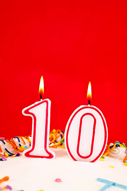 istock Decorated birthday cake with number 10 burning candles.  Red background 182424423