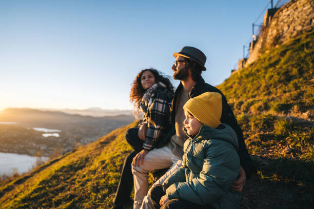 Family enjoys time together on mountain top Family sits on mountain top together and looks out to lake and sunset potential energy stock pictures, royalty-free photos & images