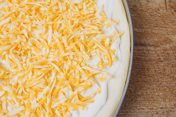 An unbaked beginning to a breakfast pizza with a bread dough crust, alfredo sauce and shredded monterey jack and colby cheese.