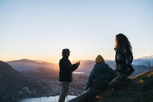 Family takes photo of son and mother on mountain top above lake at sunset