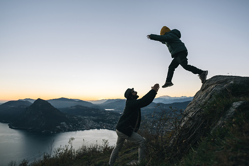 Son jumps into fathers arms on mountain top above lake at sunset