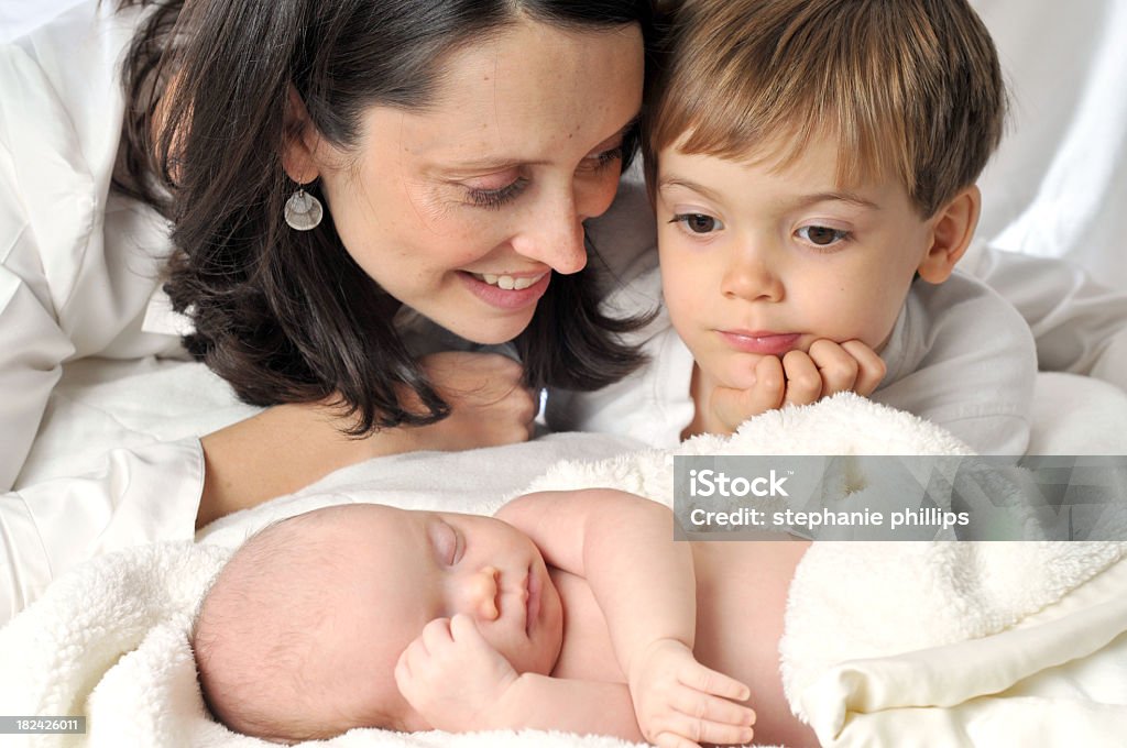 Mother and Son looking at Sleeping Infant Lying on Bed Horizontal image of a mother and her two children. A newborn baby sleeps quietly as her mother and older brother look on. The older brother seems a little curious about the new sister, and it appears the mother is trying to talk to him about this. Adult Stock Photo