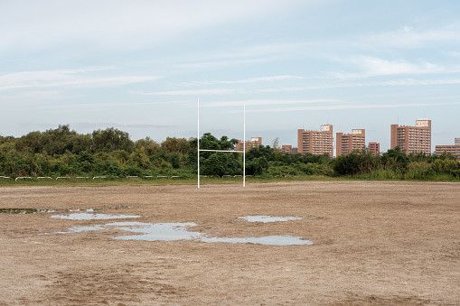 Part of a sandy sports field with goal post and puddles on an overcast day.