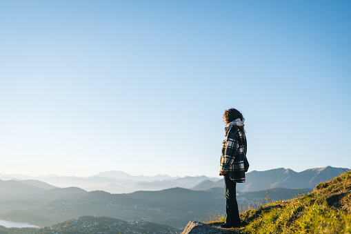 Young woman stands on mountain top and looks across mountain ranges and lake