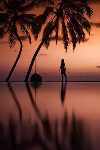 Silhouette of a carefree woman walking at the edge of infinity pool on the beach at sunset. Copy space.