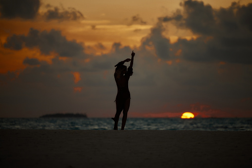 Silhouette of carefree woman having fun while dancing with raised arms during summer sunset on the beach. Copy space.