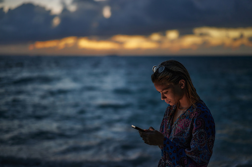 Carefree woman text messaging on cell phone during summer evening on the beach. Copy space.
