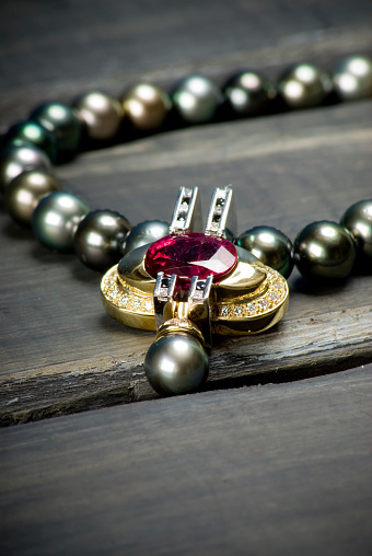 Up-close studio shot of a mulit colored pearl necklace with ruby pendant on wooden surface.