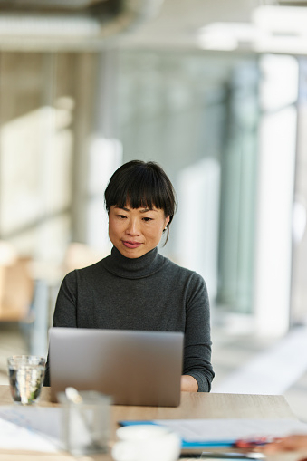 Smiling Japanese businesswoman reading an e-mail on a computer in the office.