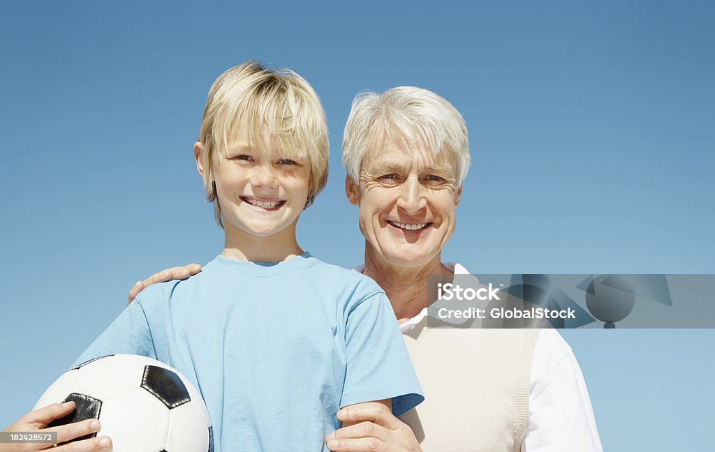 Uomo con un giovane ragazzo che tiene il calcio contro il cielo blu - Foto stock royalty-free di 60-64 anni