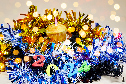 Birthday cupcake with colorful tinsel and happy new year 2024, bokeh light on a beige background