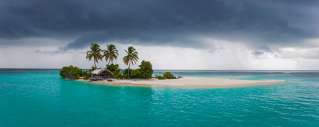 Hangnaameedhoo, Northern Ari Atoll, Republic of Maldives - June 06, 2008:  Picturesque Maldivian Island with a lagoon, sheltered hut, lush vegetation, and three coconut palm trees captured in a photograph moments before a monsoon tropical storm struck. Unfortunately, the island succumbed to nature's fury in the years following this photograph, transforming into a bare sandbank without vegetation