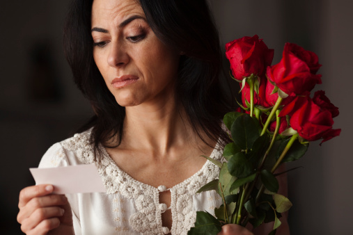 Woman is holding a roses bunch and reading a card with sneer expression. Focus on face.