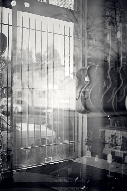 Electric guitars are visible hanging through a store front window, the glass clouded by reflections of the trees behind.  Vertical with copy space.