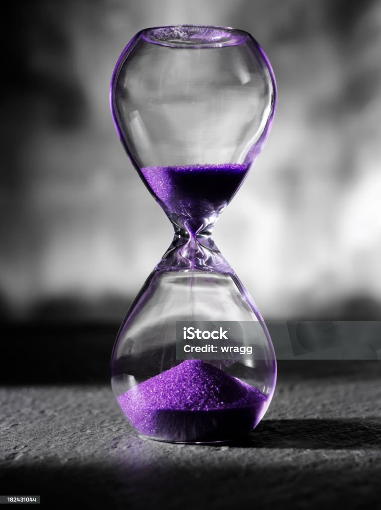 Purple Falling Sand in a Hourglass Purple sand falling through a hourglass, standing on slate.  Hourglass Stock Photo