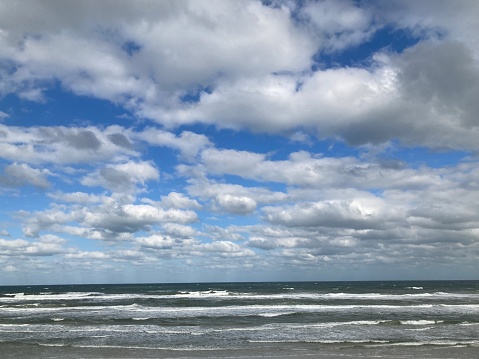 A cloudscape fills a blue sky above the ocean waves and white caps