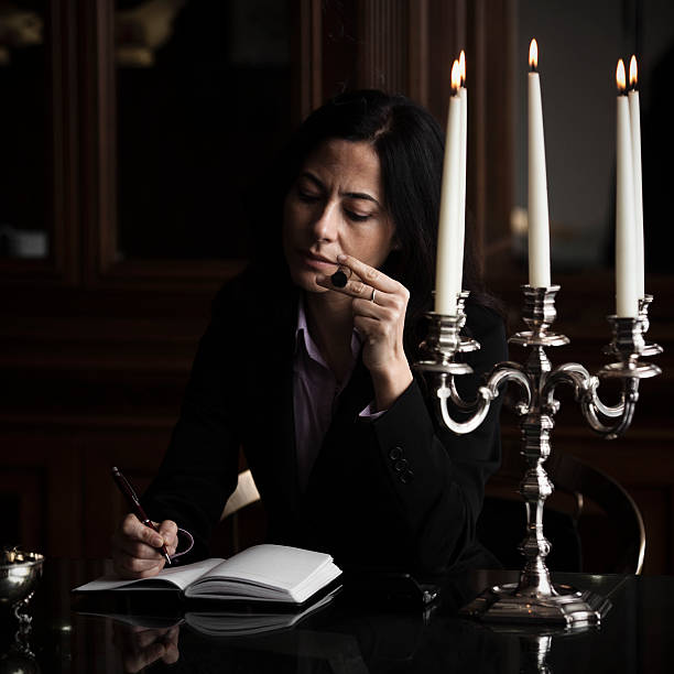 Businesswoman Posh businesswoman writing in her diary and smoking a cigar. Low key. Focus in the hand with cigar. Soft focus. smoking women luxury cigar stock pictures, royalty-free photos & images