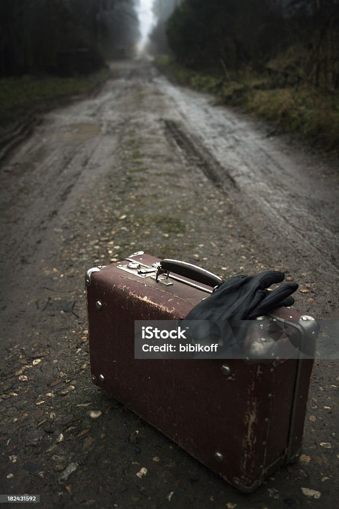 Road is calling old worn suitcase with gloves on a foggy country road Night Stock Photo