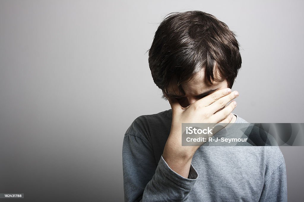 Depression "Young male with head in his hand, sombre tone." Teenage Boys Stock Photo