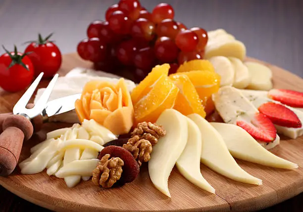 "A delicious selection of cheese served with grape, tomatoes, strawberry, orange, walnut, apricot on the cheese plate"