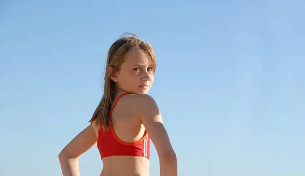 Child in sports top looking over her shoulder, against a blue sky