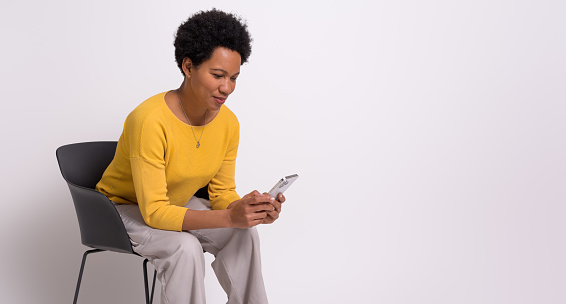Confident female entrepreneur texting over smart phone while sitting on chair over white background