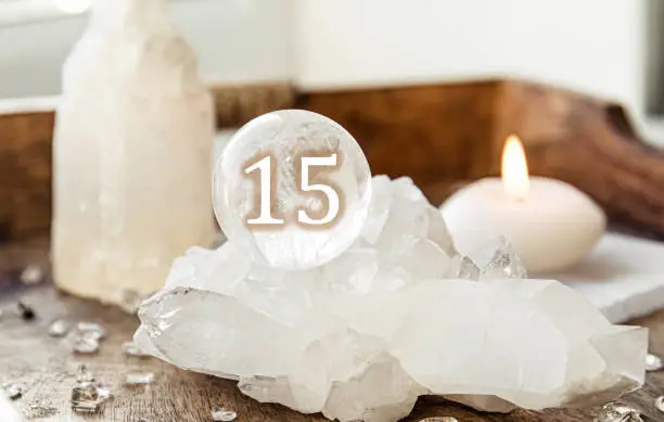 Number fifteen on Gemstone sphere or crystal balls known as crystallum orbis and orbuculum. Natural clear quartz ball on stand on wood tray in home. Predictions concept.
