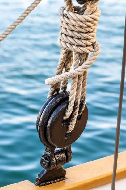 Close-up of standing rigging rope tied to black oiled deadeye with water ripples in background