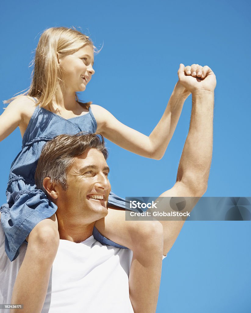 Padre llevando a su hija en hombros contra el cielo azul - Foto de stock de 30-39 años libre de derechos