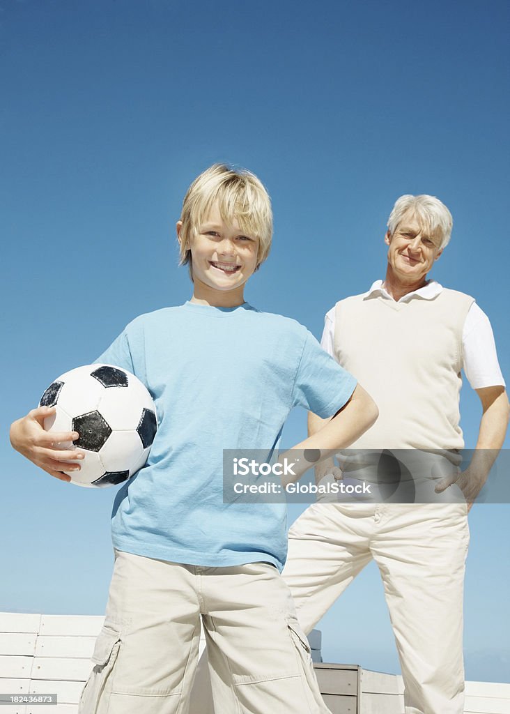 Garoto segurando uma bola de futebol com seu avô em segundo plano - Foto de stock de 60-64 anos royalty-free