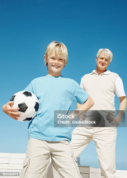 Foto de Garoto Segurando Uma Bola De Futebol Com Seu Avô Em Segundo Plano e mais fotos de stock de 60-64 anos