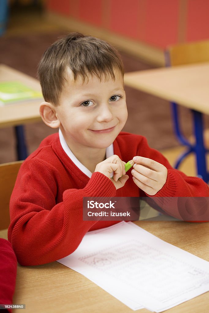 Happy School Boy Sitting At His Desk Close up of a school boy sitting at his desk and smiling at camera. Red Stock Photo