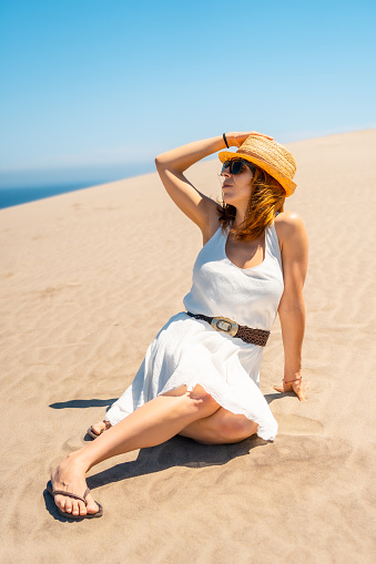 Vertical photo of a Woman holding sun hat sitting outdoors on a windy day in Cabo de Gata, Spain